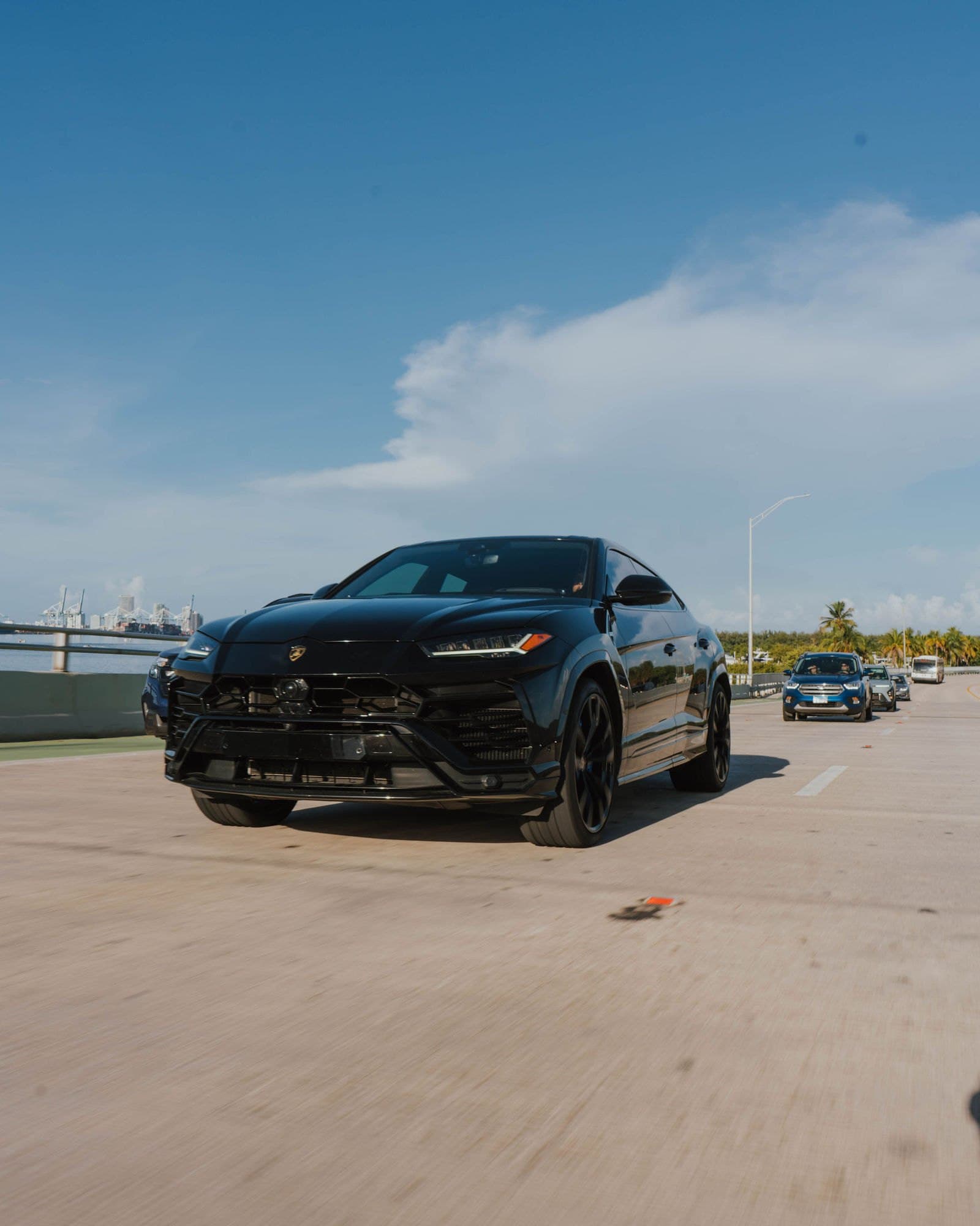 Black Lamborghini Urus driving with the Miami skyline behind