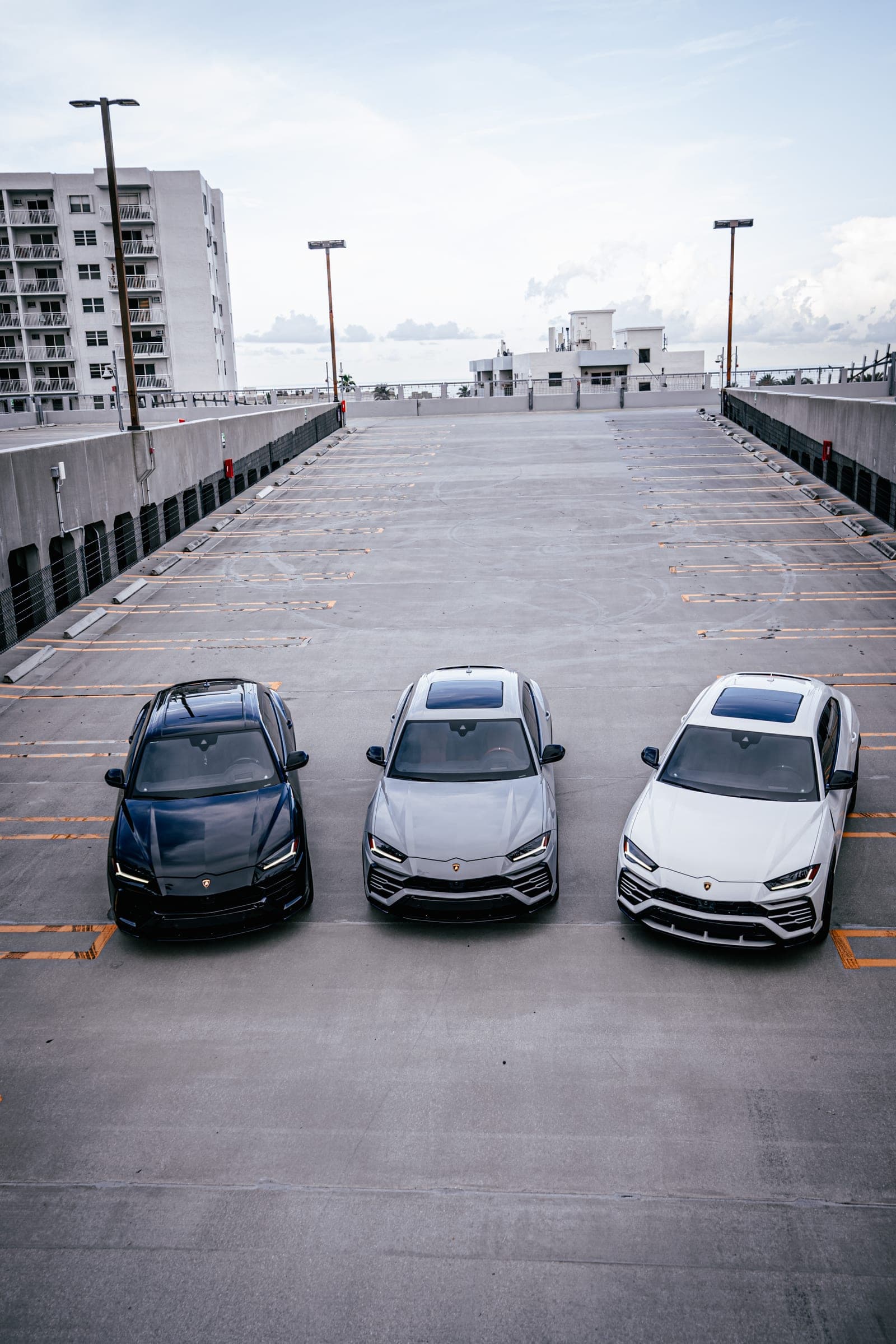 Black, grey and white Lamborghini Urus SUVs parked together on a Miami rooftop