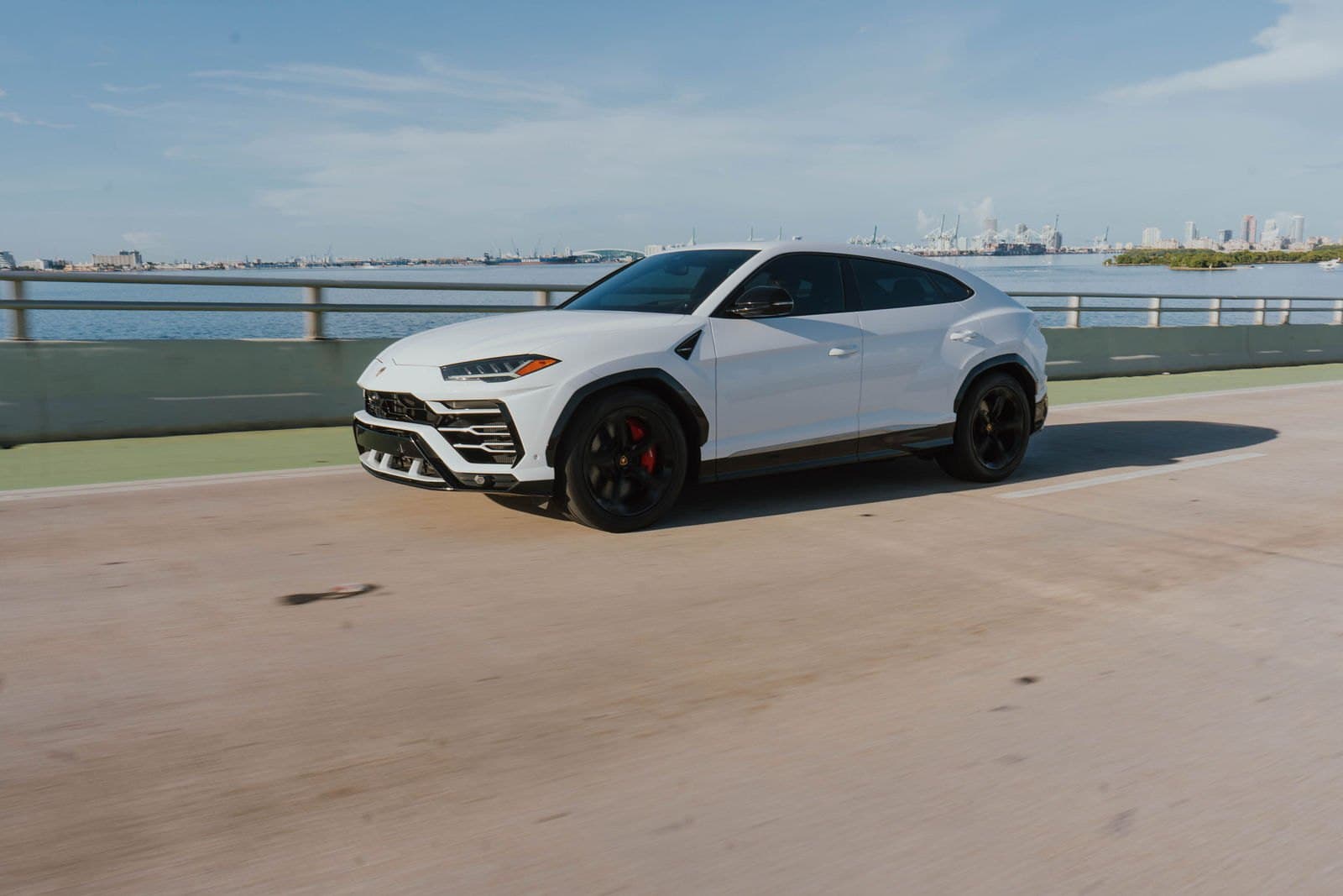 White Lamborghini Urus driving along the Rickenbacker Causeway with the Miami skyline behind